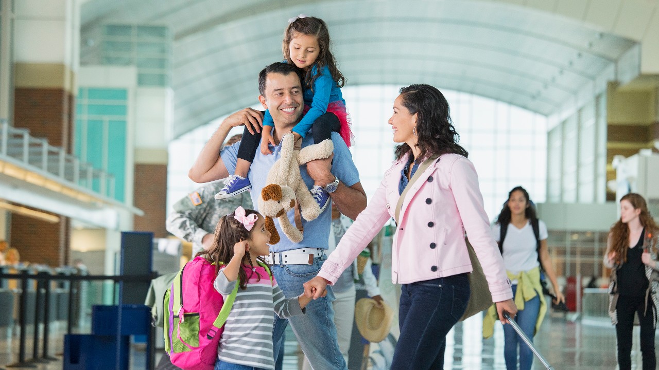 a couple of young parents with two girls happily walking in an airport with luggages