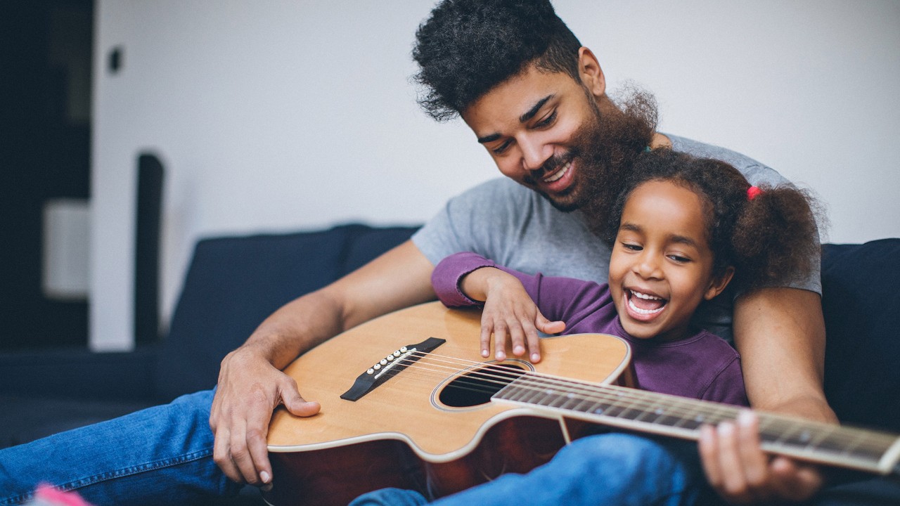 a father happily holding an acoustic guitar together with his daughter; image used for HSBC Mauritius savings account page